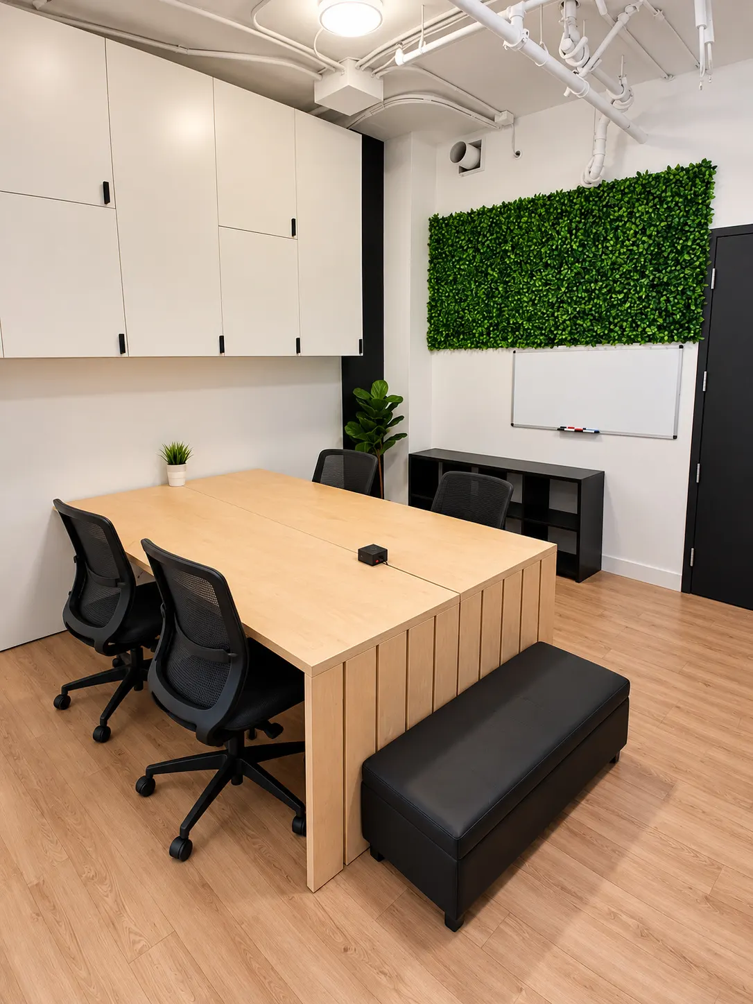Private office 106-1B at 2727 Coworking, Griffintown: pale oak shared table with four mesh chairs, a padded bench, a green foliage wall and a whiteboard