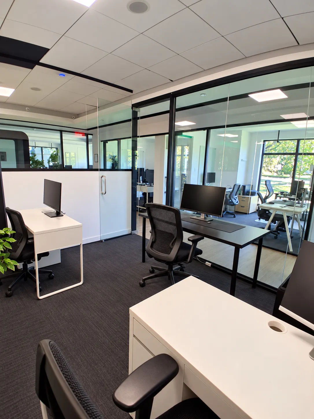 Private office 109-6 at 2727 Coworking, Griffintown: white and black desks inside black-framed glass walls, with windows visible across the floor.
